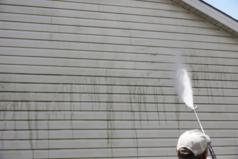 A man rinsing his steel siding with a power washer after scrubbing from top to bottom.