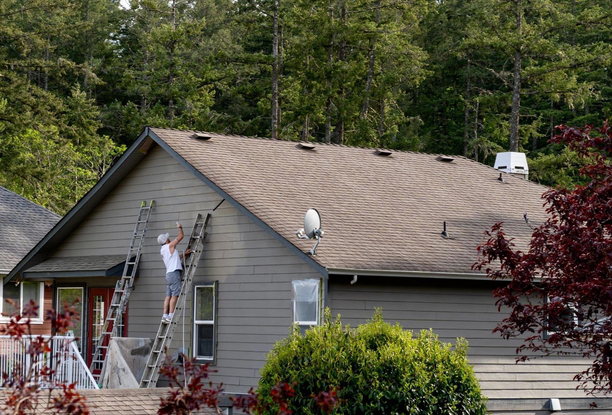 A professional is spray painting a house with metal siding.